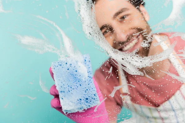 Hombre borroso en guante de goma vidrio de limpieza con esponja aislada en azul - foto de stock
