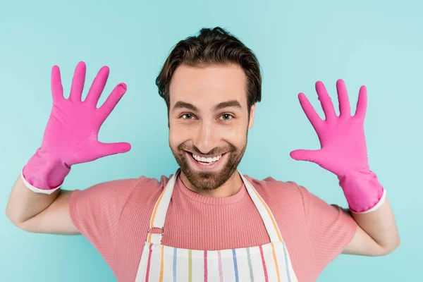 Hombre positivo en guantes de goma y delantal mirando a la cámara aislada en azul - foto de stock