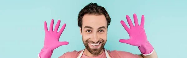 Positive man in rubber gloves looking at camera isolated on blue, banner — Stock Photo