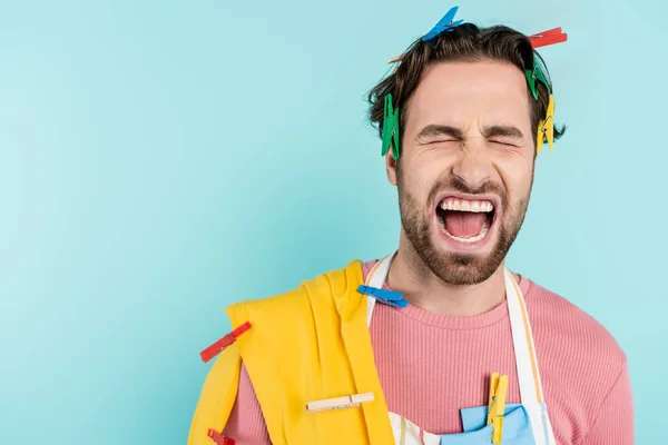 Enojado hombre soltero en pinzas de ropa gritando aislado en azul — Stock Photo