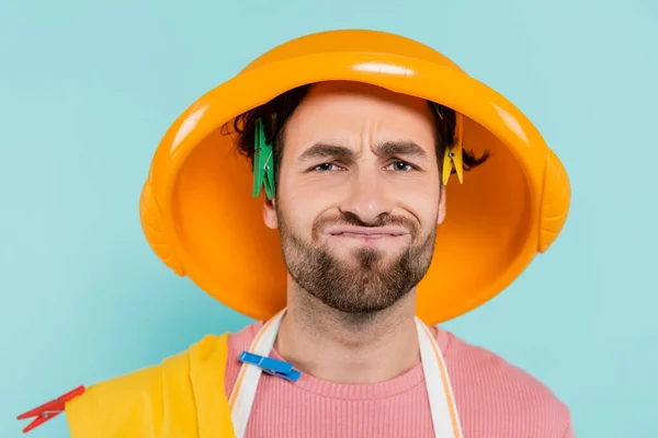 Dissatisfied man in clothespins and wash bowl on head isolated on blue — Stock Photo