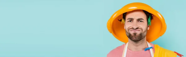 Upset unmarried man in clothespins and wash bowl on head looking at camera isolated on blue, banner — Stock Photo