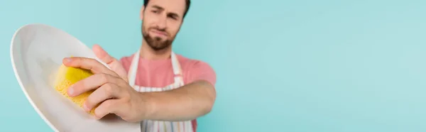 Blurred man cleaning plate with sponge isolated on blue, banner — Stock Photo