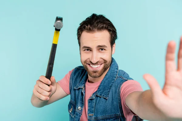 Homme souriant regardant la caméra tout en tenant le marteau isolé sur bleu — Photo de stock