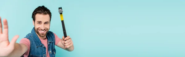 Positive man in denim vest holding hammer isolated on blue, banner — Stock Photo