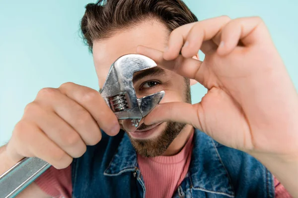 Junger Mann hält Schraubenschlüssel in der Hand und blickt vereinzelt in die Kamera — Stockfoto