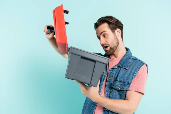 Hombre sorprendido mirando la caja de herramientas abierta aislada en azul - foto de stock