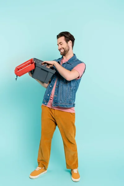 Full length of positive man looking at open toolbox on blue background — Stock Photo