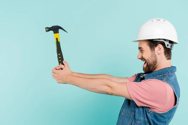 Side view of excited man in hardhat holding hammer isolated on blue — Stock Photo