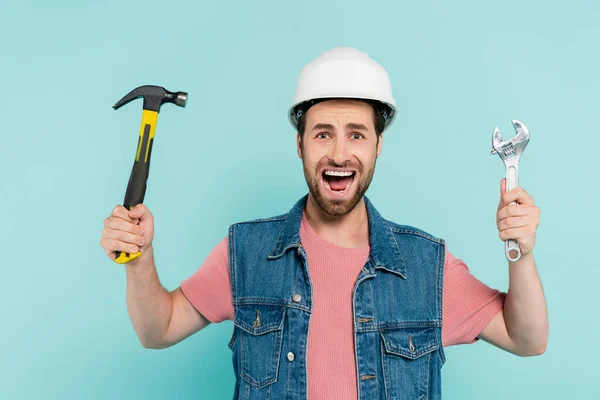 Urlando uomo in hardhat tenendo martello e chiave isolata su blu — Foto stock