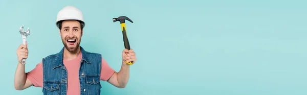 Urlando uomo in casco tenendo martello e chiave isolata su blu, banner — Foto stock