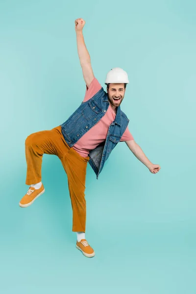 Piena lunghezza di uomo positivo in casco e gilet di denim guardando la fotocamera su sfondo blu — Foto stock