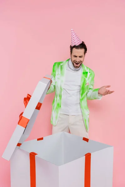 Hombre sorprendido en la apertura de la tapa del partido caja de regalo grande aislado en rosa - foto de stock