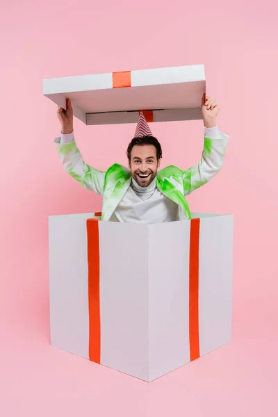 Homme joyeux dans la casquette de fête tenant chapeau de grande boîte-cadeau sur fond rose — Photo de stock