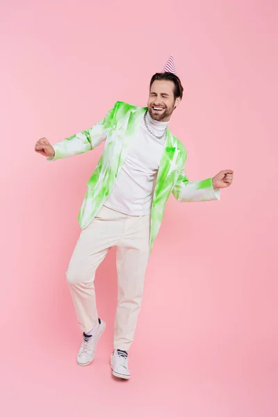 Allegro uomo in berretto partito e giacca ballare su sfondo rosa — Foto stock