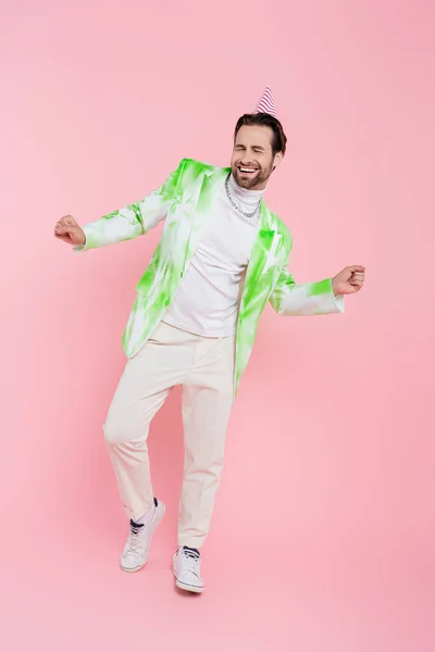 Homme joyeux en chapeau de fête et veste dansant sur fond rose — Photo de stock