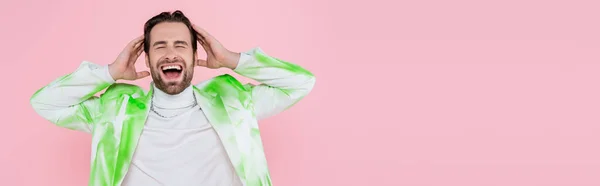 Hombre gritando en chaqueta elegante tocando la cabeza aislado en rosa, bandera - foto de stock