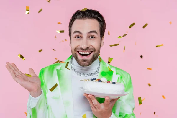 Allegro uomo che tiene la torta di compleanno sotto i coriandoli su sfondo rosa — Foto stock