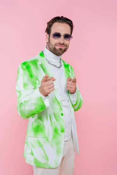 Hombre con estilo en gafas de sol apuntando a la cámara aislada en rosa - foto de stock