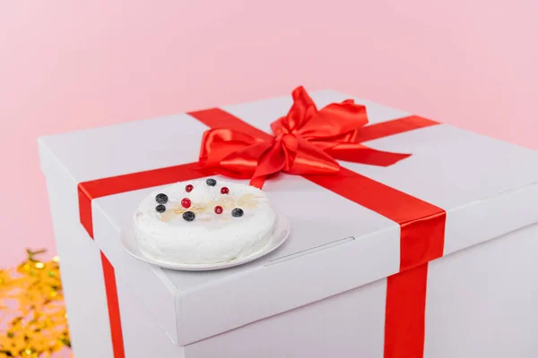 Gâteau d'anniversaire sur une énorme boîte cadeau près de confettis flous sur fond rose — Photo de stock