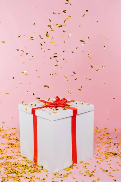 Big gift box under falling confetti on pink background — Stock Photo