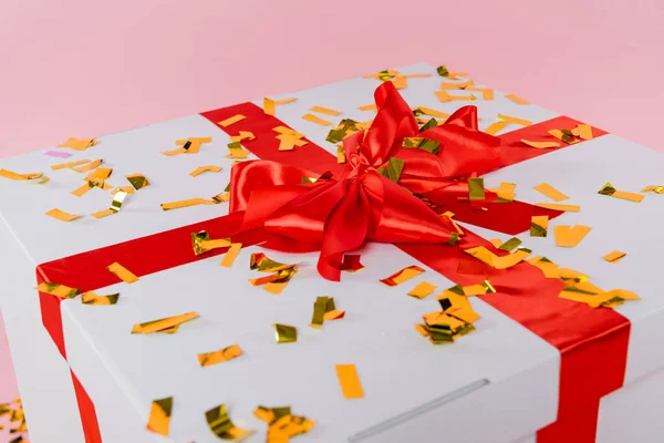 Ігристе конфетті на подарунковій коробці з бантом на рожевому фоні — стокове фото