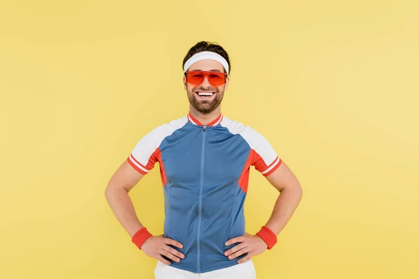 Веселий спортсмен в сонцезахисних окулярах тримає руки на стегнах ізольовані на жовтому — стокове фото