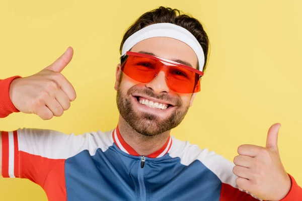 Happy sportsman in sunglasses showing thumbs up isolated on yellow — Stock Photo