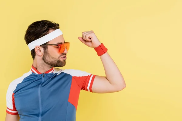 Deportista morena en gafas de sol mirando los músculos aislados en amarillo - foto de stock