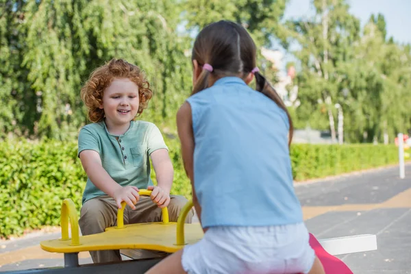 Alegre chico cabalgando balancín con hermana en verano parque - foto de stock