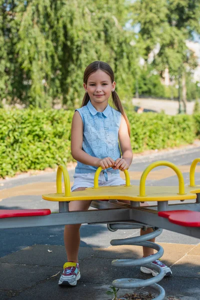 Chica feliz mirando a la cámara mientras monta balancín en el parque - foto de stock