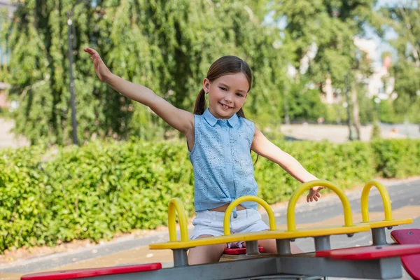 Excitée fille regardant caméra tout en chevauchant balançoire avec les mains tendues — Photo de stock