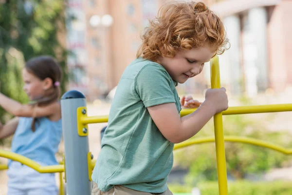 Curly boy playing near blurred girl on playground — Stock Photo
