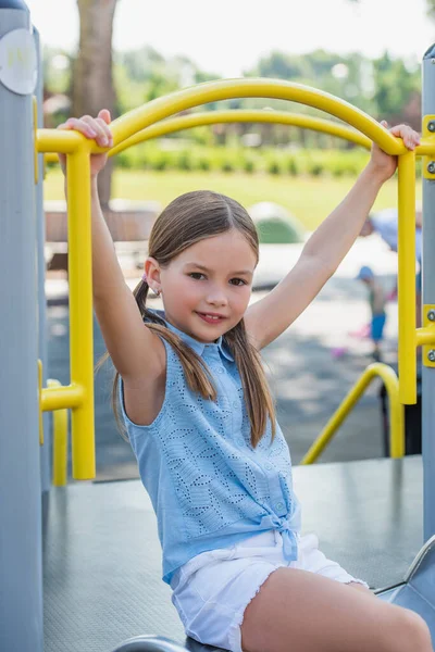 Lächelndes Mädchen, das in die Kamera schaut, während es Spaß auf dem Spielplatz hat — Stockfoto