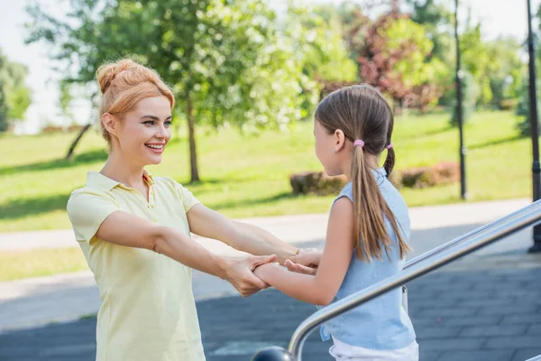 Smiling woman holding hands of daughter while spending time outdoors — Stock Photo