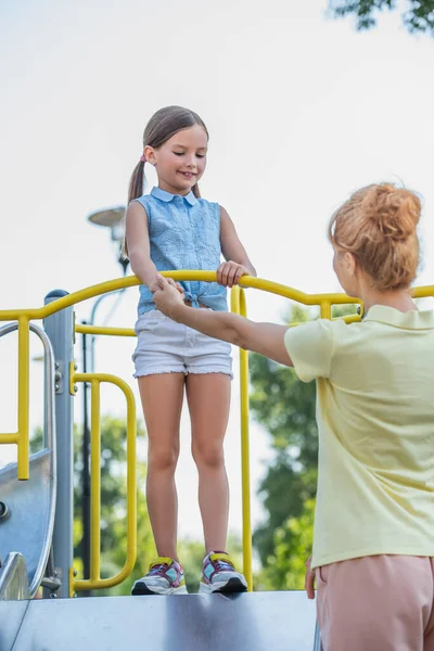 Woman holding hand of daughter standing on slide in amusement park — Stock Photo