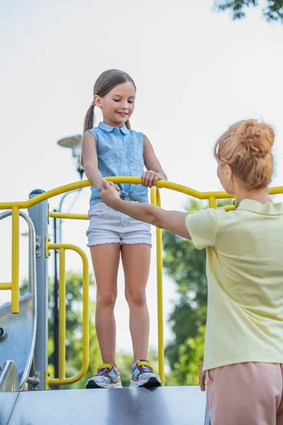 Femme tenant la main de fille debout sur la glissière dans le parc d'attractions — Photo de stock