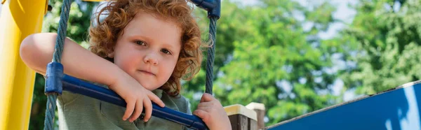 Boy looking at camera from rope ladder in amusement park, banner — Stock Photo