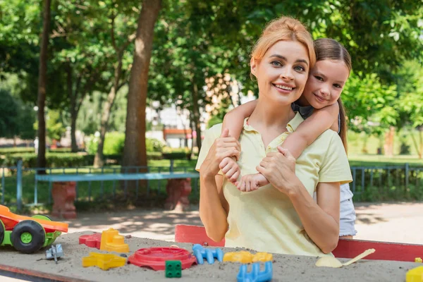 Mädchen umarmt glückliche Mutter in der Nähe von buntem Spielzeug, während sie Zeit auf dem Spielplatz verbringt — Stockfoto