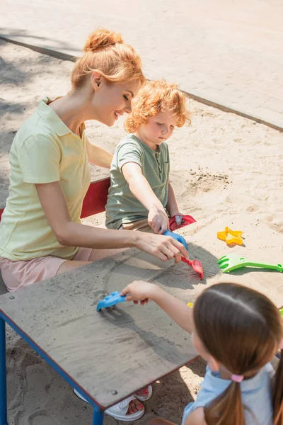 Lächelnde Frau und Kinder, die draußen mit Harken und Sand spielen — Stockfoto