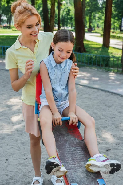 Woman smiling near daughter riding seesaw on playground — Stock Photo