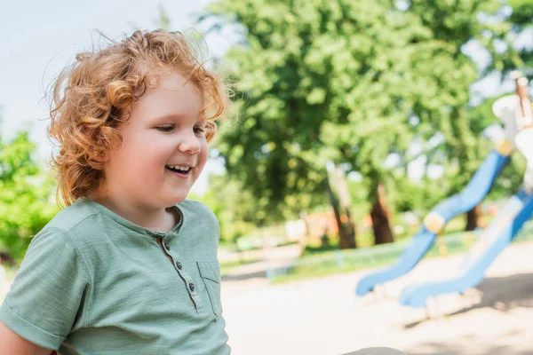 Кудрявый мальчик в футболке улыбается на улице в парке — стоковое фото