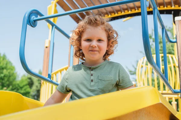 Vista de ángulo bajo del niño en la diapositiva mirando la cámara en el patio de recreo - foto de stock