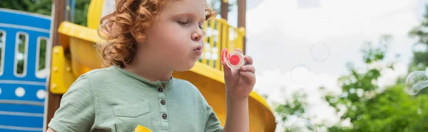 Lockenkopf pustet Seifenblasen, während er Zeit im Freien verbringt, Banner — Stockfoto