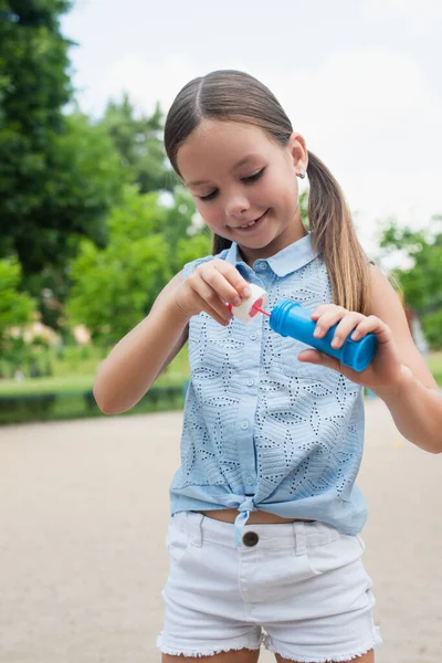 Cheerful girl holding bottle and bubble blower outdoors — Stock Photo