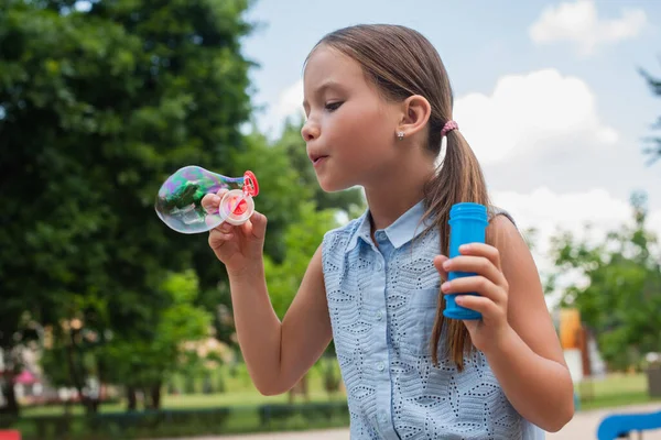 Ragazza in camicetta senza maniche che soffia bolla di sapone nel parco — Foto stock