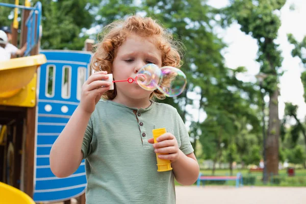 Lockenkind pustet Seifenblasen auf Spielplatz — Stockfoto