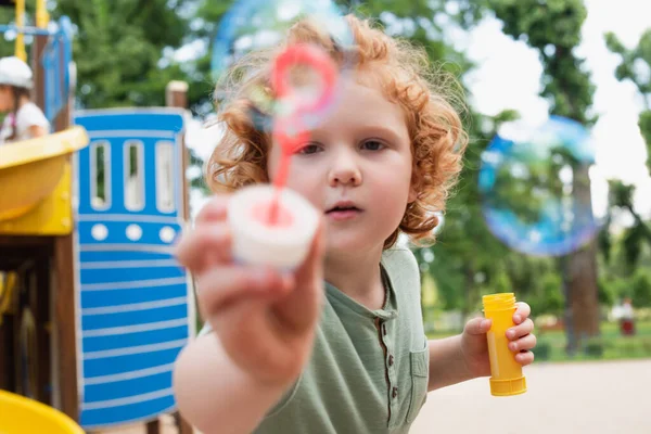 Redhead boy looking at camera and showing blurred bubble blower — Stock Photo