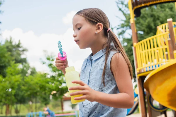 Mädchen in ärmelloser Bluse pustet Seifenblasen auf Spielplatz — Stockfoto