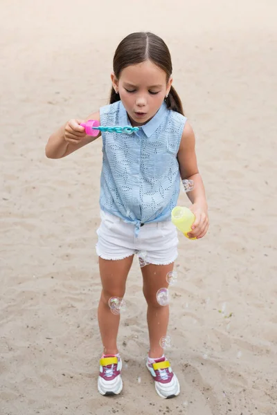 Full length view of girl in shorts blowing soap bubbles outdoors — Stock Photo
